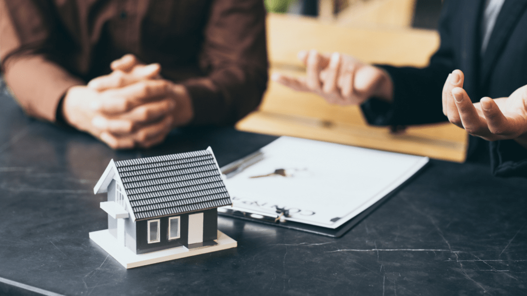 two people sitting at a table with a house model in front of them