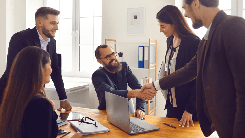 two people shaking hands in front of a laptop