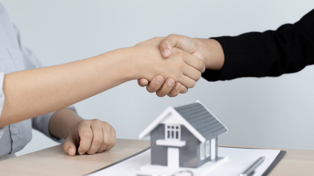 two people shaking hands over a house model