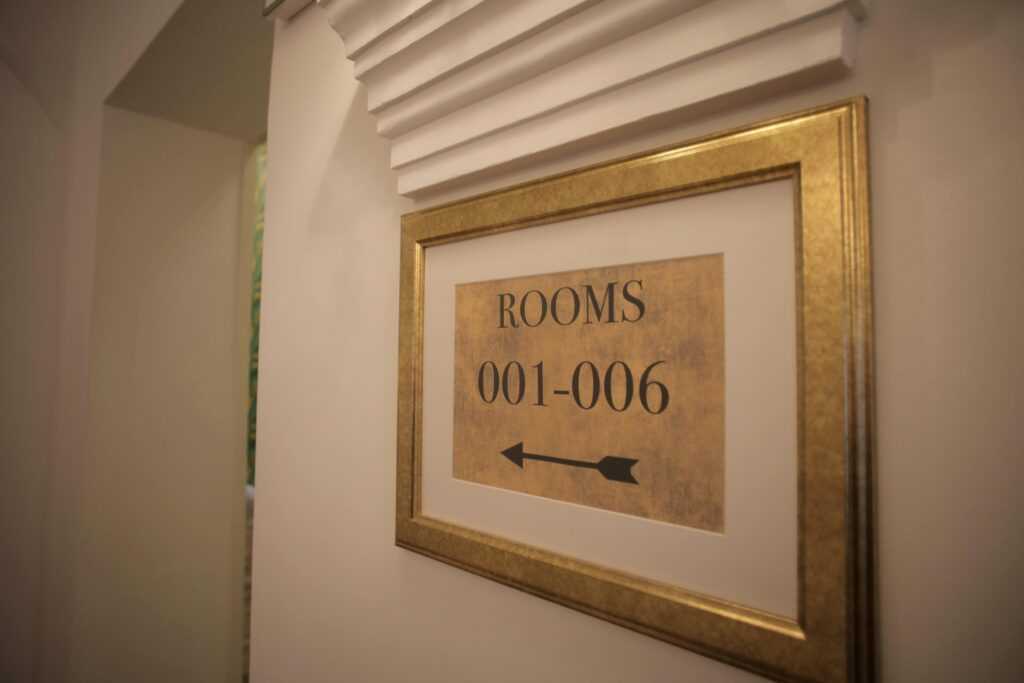 Classic hotel sign indicating directions to rooms 001 to 006 with a gold frame for a luxurious interior decor.
